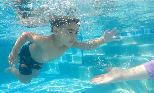 Boy swimming underwater reaching for an outstretched hand in the pool.