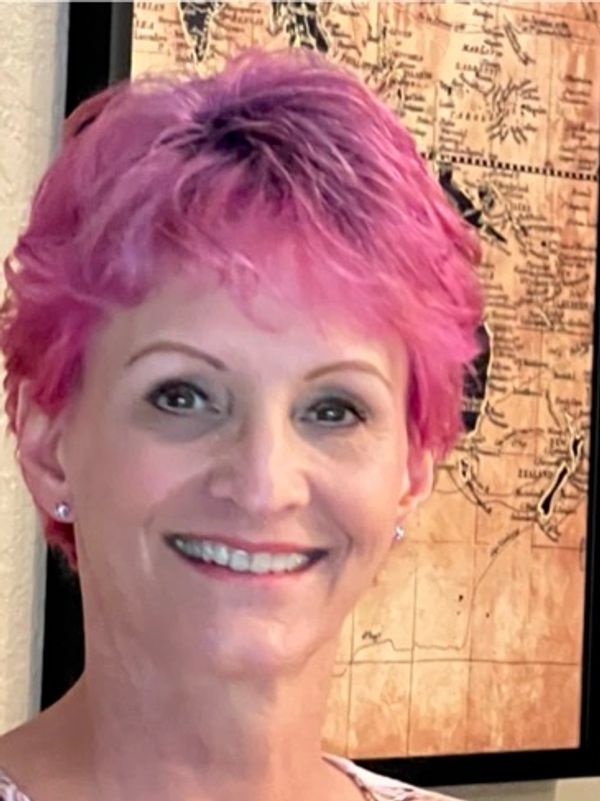 Smiling woman with vibrant pink hair in front of a vintage map.