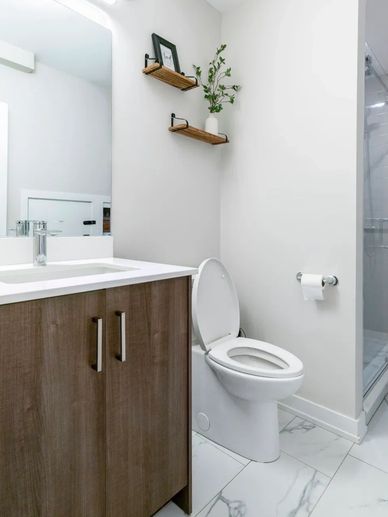 Modern bathroom with wooden cabinet, white toilet, and minimalist shelves.