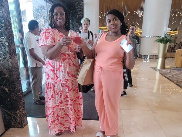 Two women smiling and toasting with drinks in a hotel lobby.