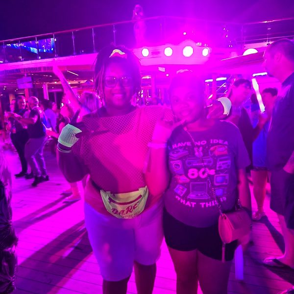 Two friends posing happily under vibrant purple lights at a crowded nighttime event.