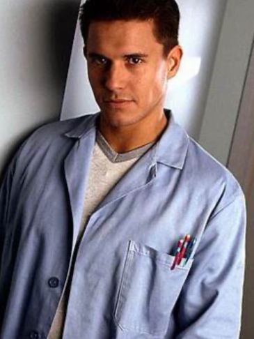 Young man in a light blue lab coat with pens in his pocket.