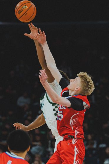Two basketball players reaching for the ball during a game.