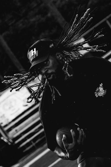 Black and white photo of a man playing football with flying dreadlocks.