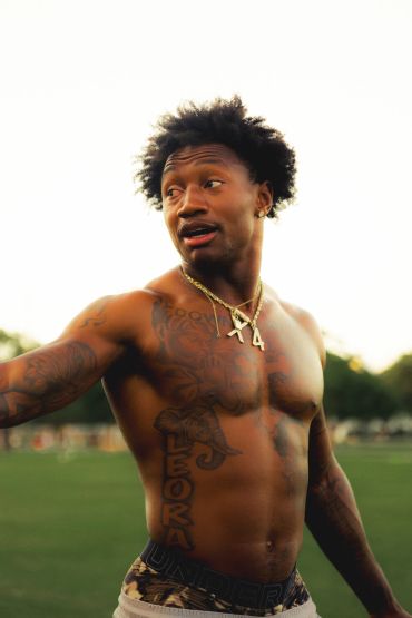 Shirtless man with tattoos and gold chains outdoors.