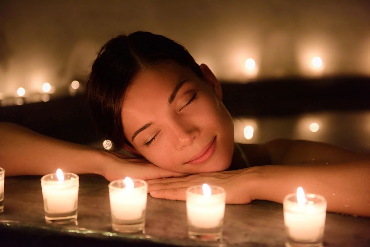 A woman relaxing in a spa with her eyes closed and votive candles burning all around her.