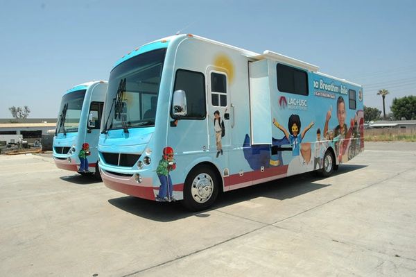 Two colorful mobile health clinic buses with cartoon characters and health messages.
