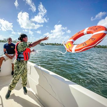 Person in uniform throws a life ring from a boat while another watches.