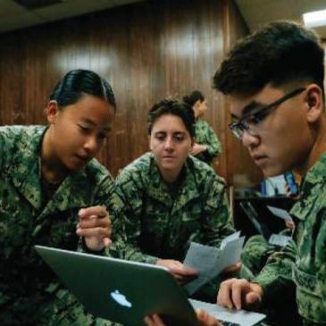 Three military personnel collaborate using a laptop.