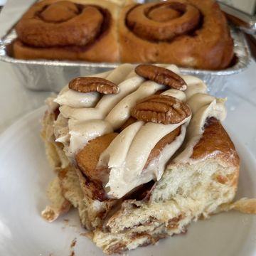 A cinnamon roll with frosting and pecans on a plate.