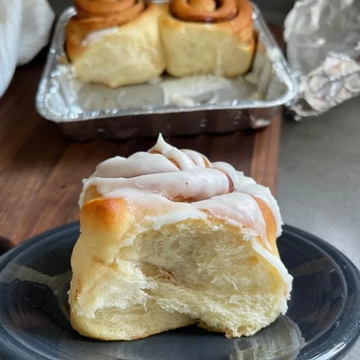 A bitten cinnamon roll on a plate with more in a tray.
