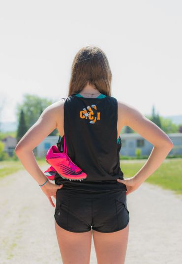 Athlete holding pink running shoes, standing on a sunny outdoor path.