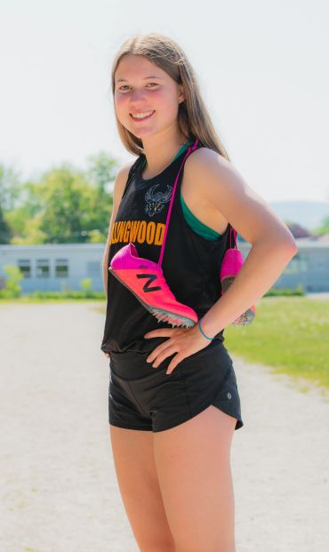 Teen girl athlete smiling with pink running shoes around her neck outdoors.