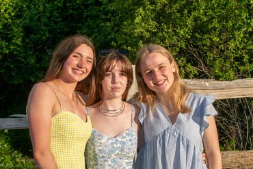 Three young women smiling outdoors in summer dresses.
