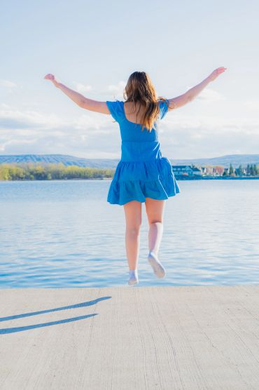 Woman jumping into a lake wearing a blue dress on a sunny day.