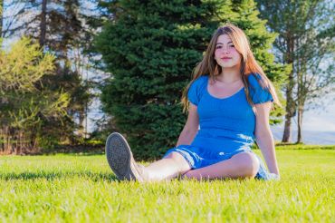 Young woman in blue dress sitting on green grass outdoors.