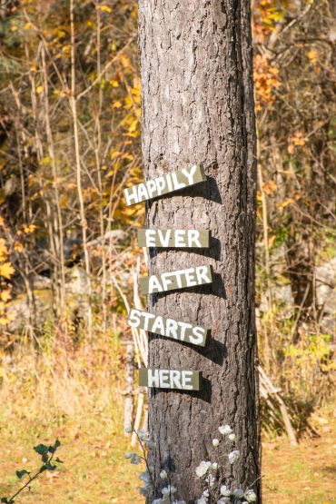 Rustic wedding sign on tree reads 'Happily Ever After Starts Here'.