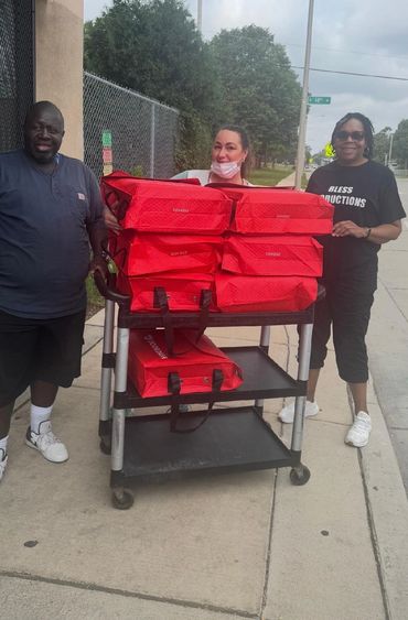 Three people with cart of red donation bags outdoors.