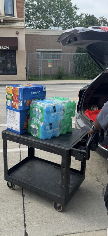 Cart with water and snacks near car trunk.