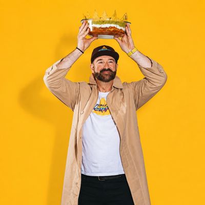 Man holding a cake above his head against a yellow background.