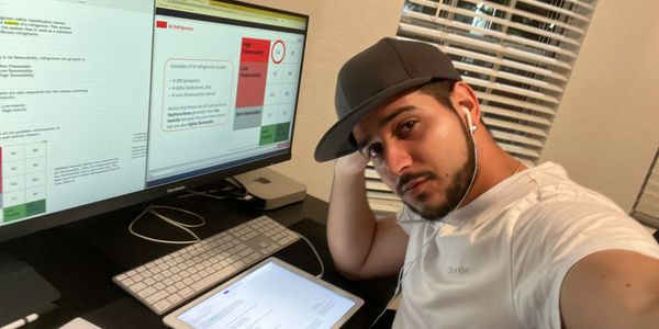A man wearing a cap and earphones works at a desk with dual monitors and a tablet.
