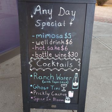 Chalkboard menu outside a restaurant listing drink specials and cocktails.
