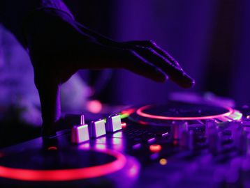 DJ hand on a glowing mixer in purple lighting.