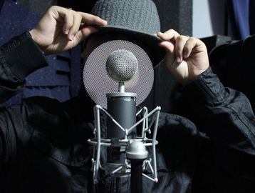 Person adjusting hat behind microphone pop filter.