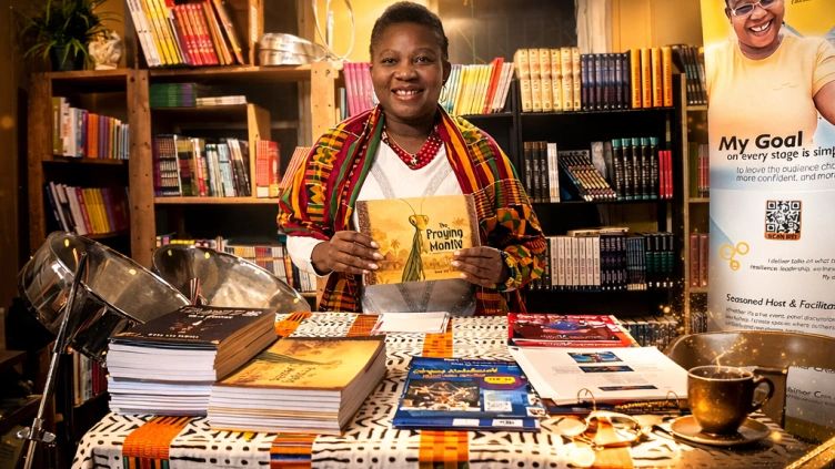 Smiling woman in traditional attire showcasing books at a table.