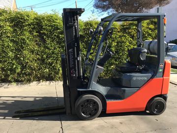 A red and gray Toyota forklift parked on a concrete surface outdoors.