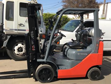 A Toyota forklift parked outdoors beside trucks.