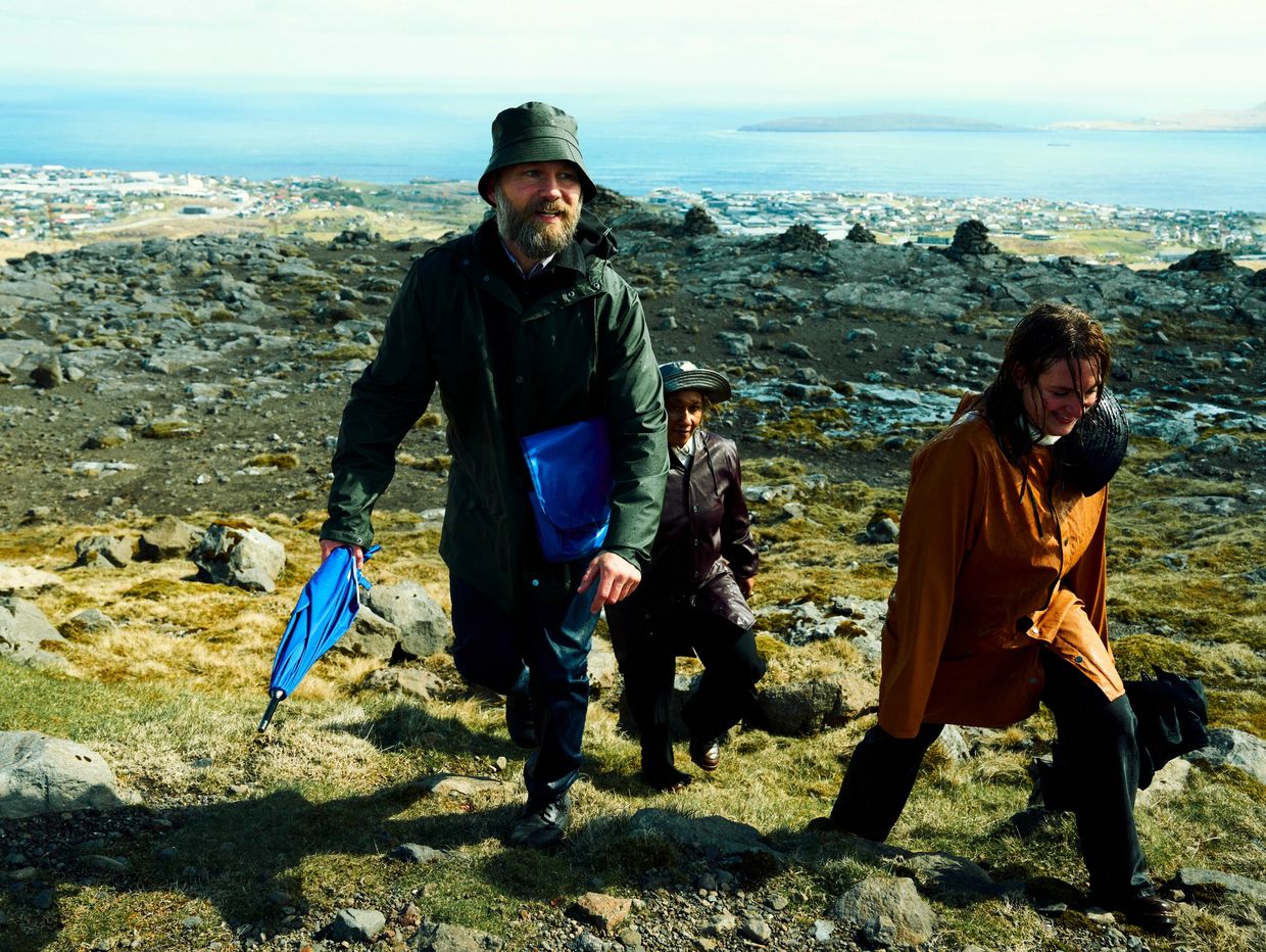 Three people hiking uphill on a rocky landscape overlooking a coastal town.