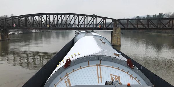 View from a boat navigating a river under a steel bridge on a cloudy day.