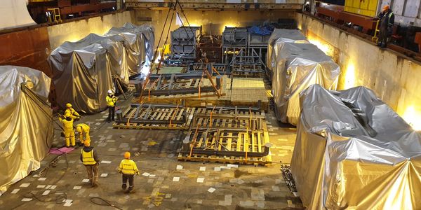 Workers assembling and covering large equipment in an industrial ship hold.