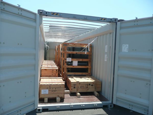 Open shipping container loaded with wooden crates and metal racks.