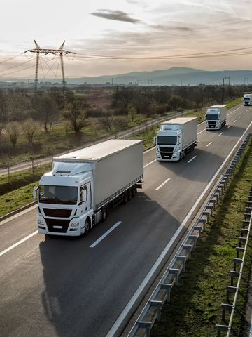 Three white cargo trucks driving on a highway during sunset.