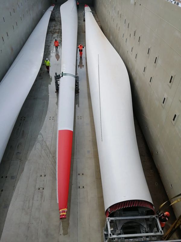Workers inspect large wind turbine blades inside a cargo hold.