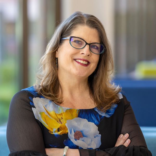 Smiling woman with glasses and floral dress.