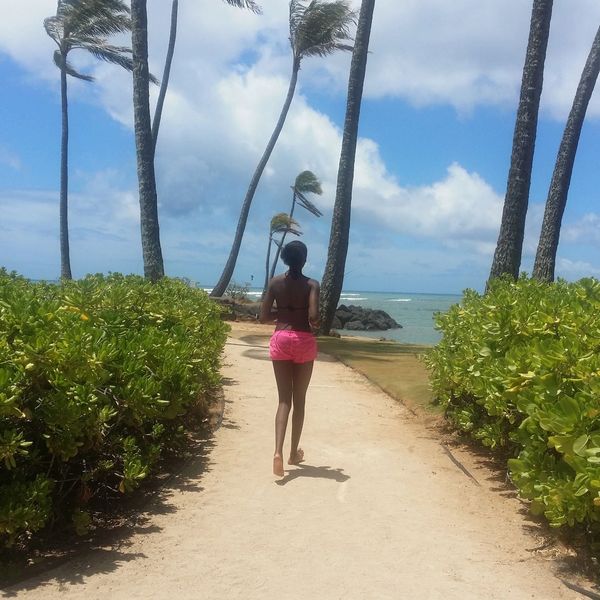 Woman walking on a sandy path by the beach with palm trees.