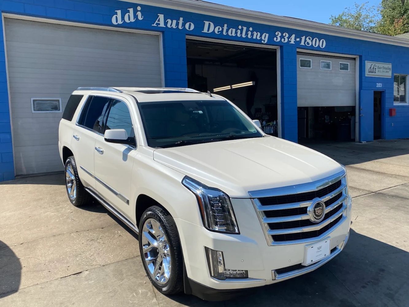 White Cadillac Escalade parked outside ddi Auto Detailing shop.