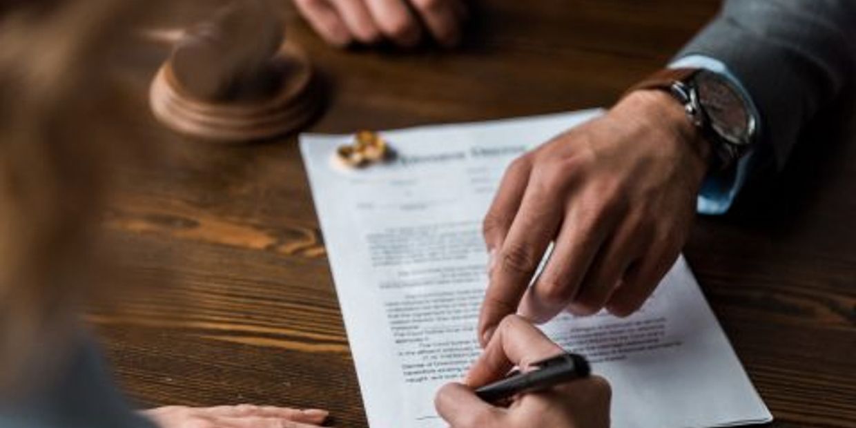 A person signing a legal document with guidance.