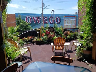 Sunny outdoor patio with chairs, plants, and a mural reading OWEGO.