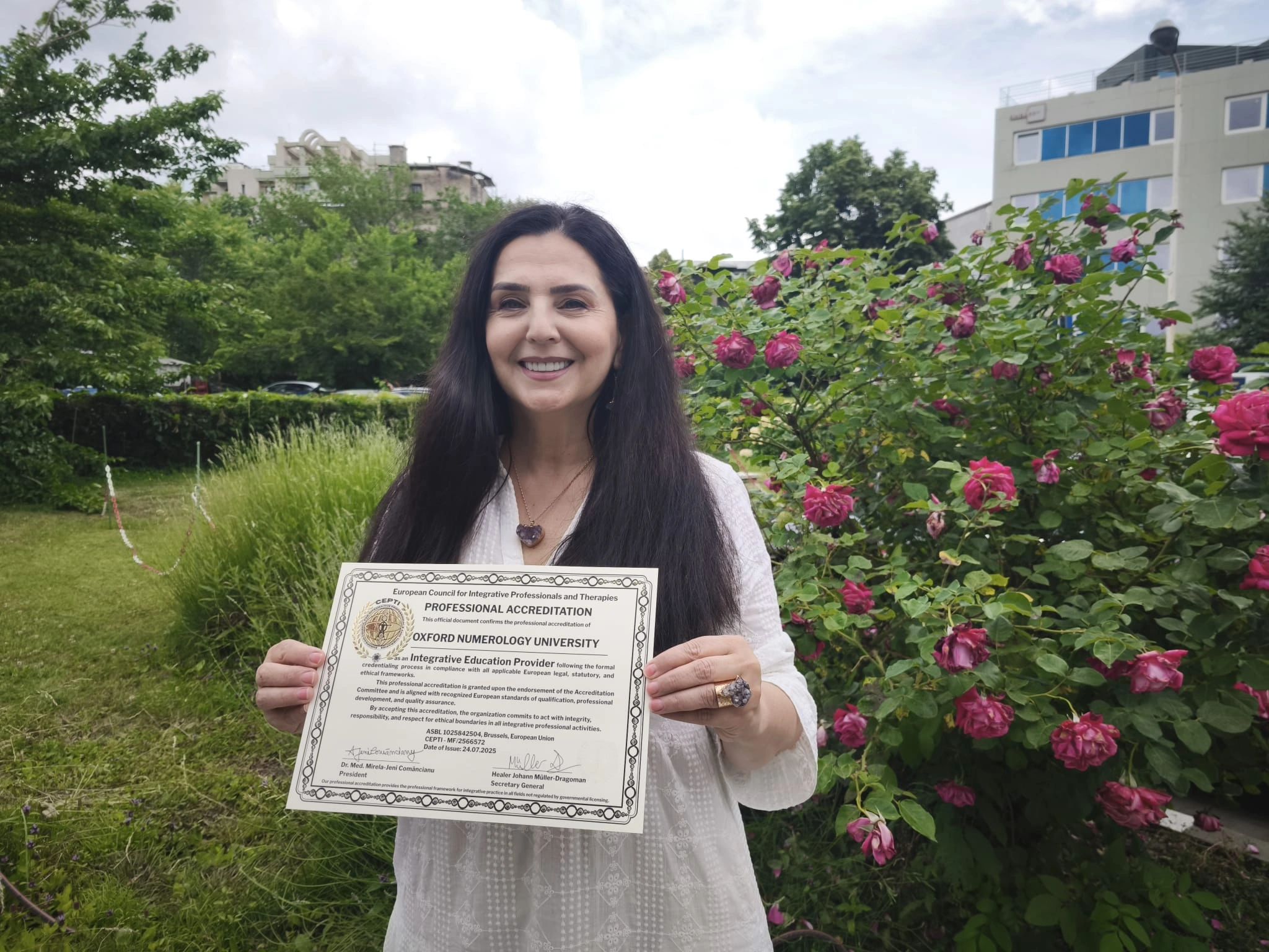 Woman holding a professional accreditation certificate outdoors with flowers.
