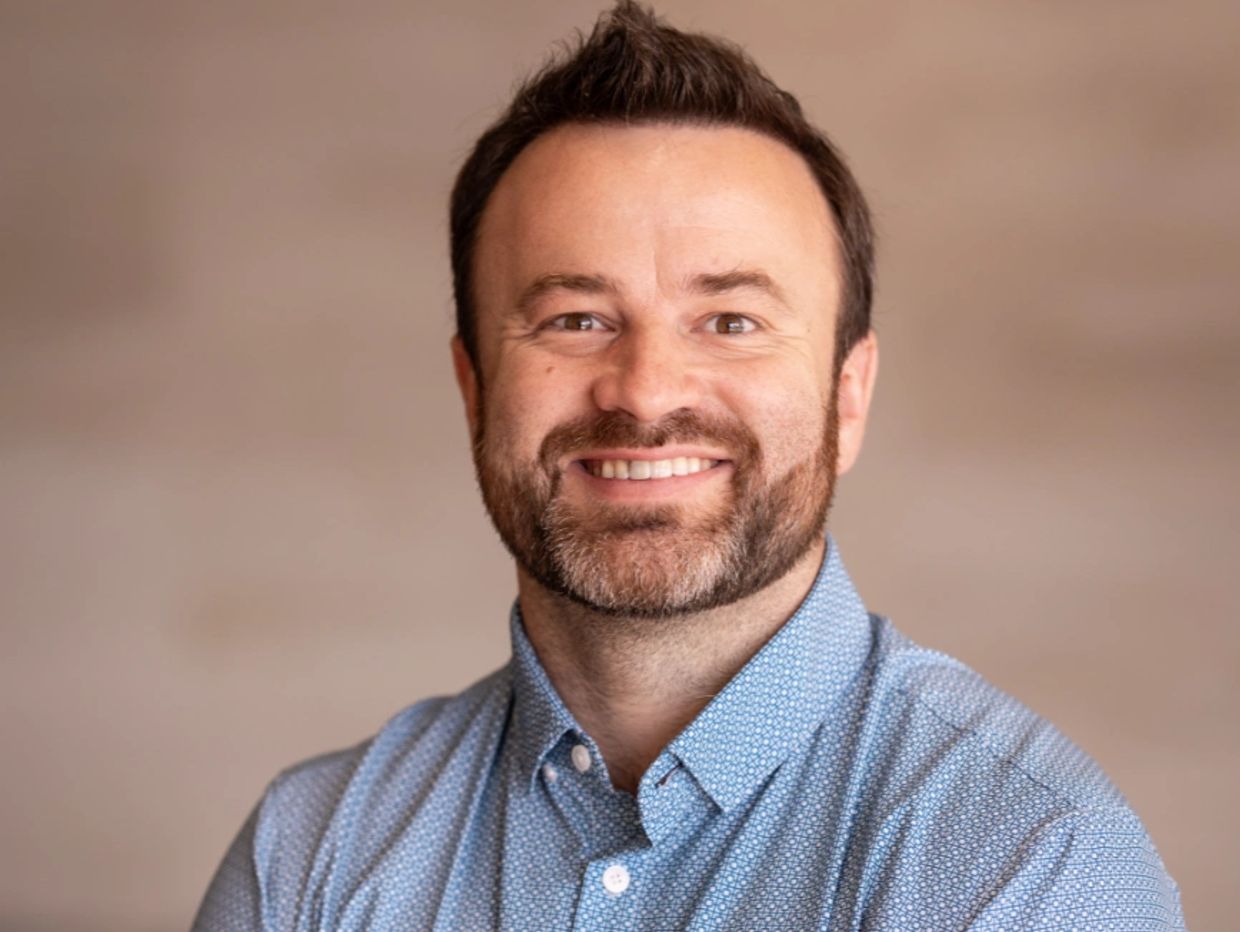 Smiling man with a beard in a blue patterned shirt.