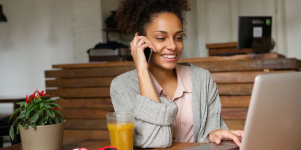 African American woman smiling while talking on her cellphone and using her laptop. 