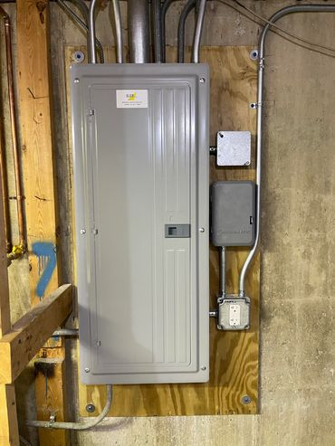 A gray electrical panel and meter installed on a wooden wall.