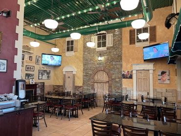 Cozy restaurant interior with stone wall, wooden chairs, and TV screens.