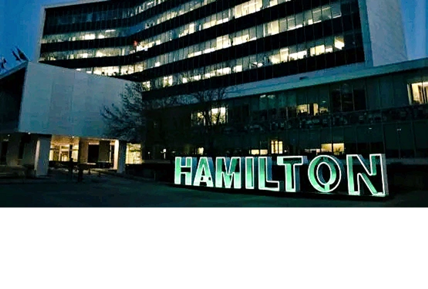 Illuminated Hamilton sign outside Hamilton City Hall at dusk.