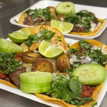 Two plates of street tacos with lime, cucumber, and fresh herbs.