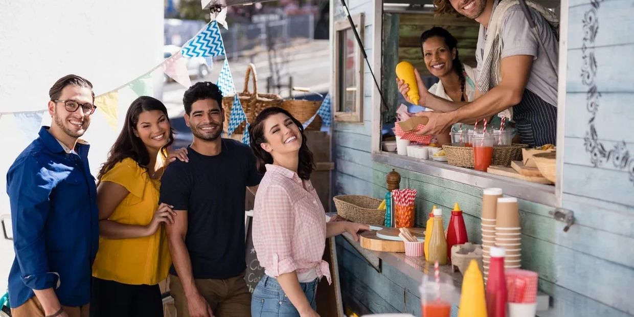 Happy friends ordering food at a colorful food truck on a sunny day.
